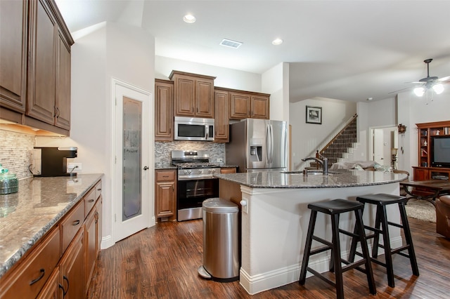 kitchen featuring appliances with stainless steel finishes, sink, a breakfast bar area, dark hardwood / wood-style flooring, and a center island with sink