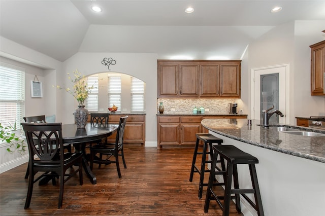 kitchen with lofted ceiling, sink, dark stone counters, and a healthy amount of sunlight