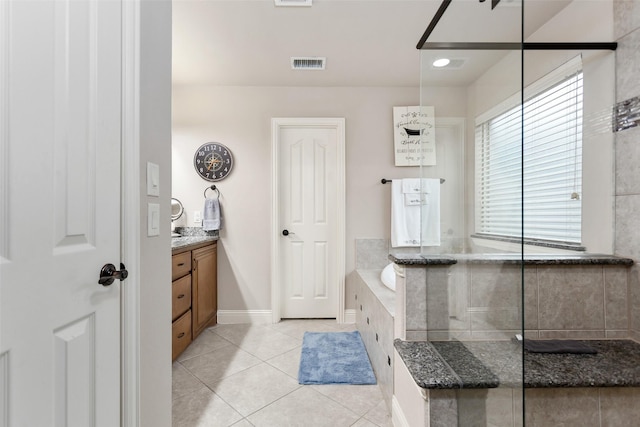 bathroom with a relaxing tiled tub, vanity, and tile patterned floors