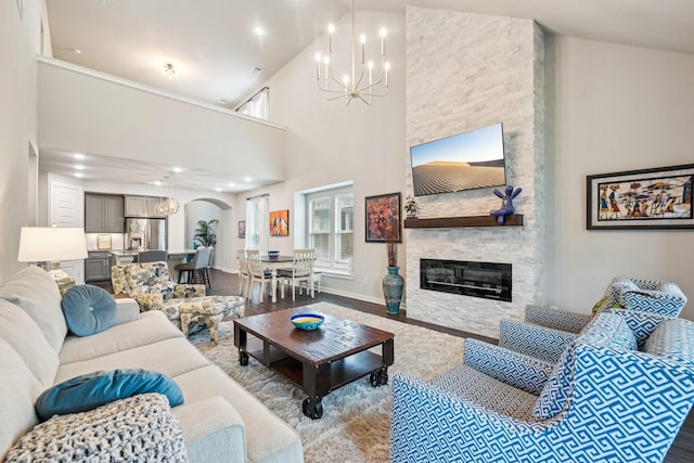 living room featuring a stone fireplace, a towering ceiling, a chandelier, and light hardwood / wood-style flooring