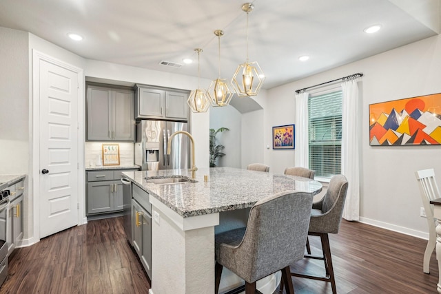 kitchen with hanging light fixtures, a kitchen island with sink, sink, and gray cabinets