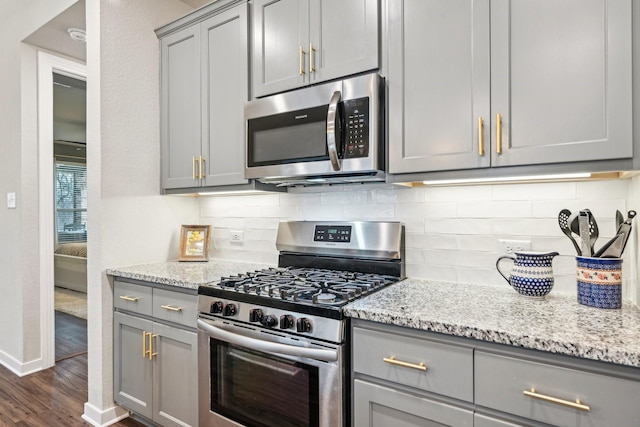 kitchen with light stone countertops, backsplash, gray cabinets, and stainless steel appliances