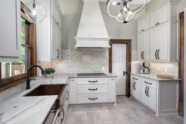 kitchen with pendant lighting, light stone counters, white cabinets, black electric cooktop, and custom exhaust hood