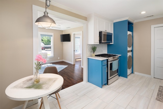 kitchen featuring white cabinetry, backsplash, stainless steel appliances, stacked washer / dryer, and blue cabinets