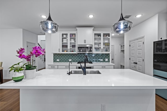 kitchen with sink, decorative light fixtures, a large island with sink, and white cabinets