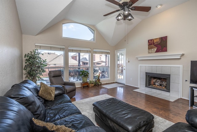 living room featuring high vaulted ceiling, wood-type flooring, a tile fireplace, and ceiling fan