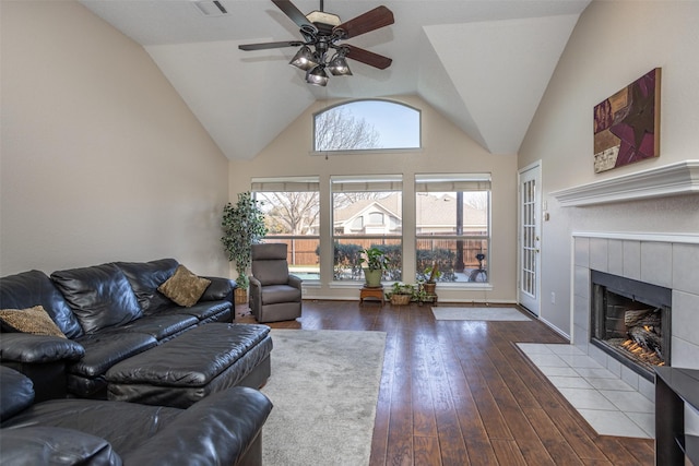 living room with ceiling fan, dark hardwood / wood-style flooring, a tiled fireplace, and high vaulted ceiling