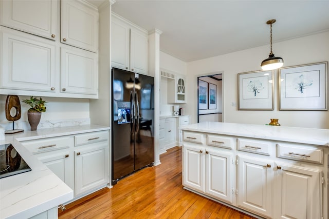 kitchen with white cabinetry, decorative light fixtures, black refrigerator with ice dispenser, and light hardwood / wood-style flooring