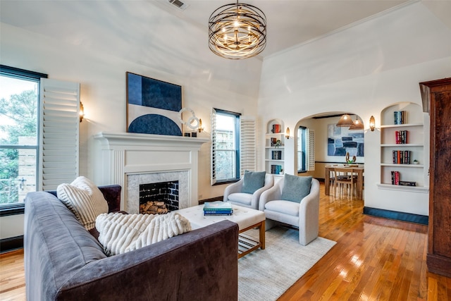 living room with built in shelves, an inviting chandelier, a high end fireplace, and light hardwood / wood-style flooring