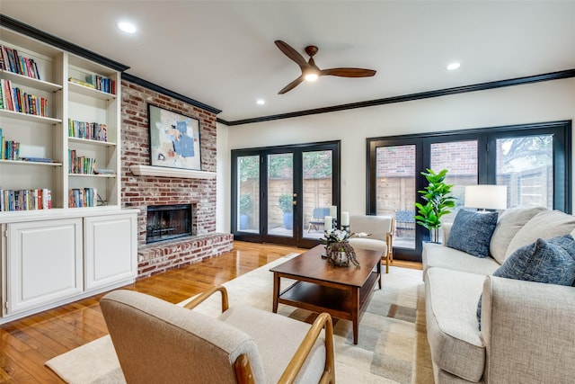 living room featuring french doors, light wood-type flooring, ornamental molding, ceiling fan, and a fireplace