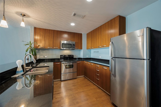 kitchen featuring hanging light fixtures, light hardwood / wood-style flooring, stainless steel appliances, and sink