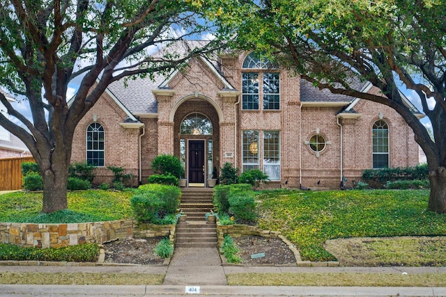 traditional-style home featuring roof with shingles, a front lawn, and brick siding