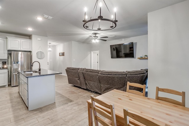 dining space featuring sink, ceiling fan with notable chandelier, and light wood-type flooring