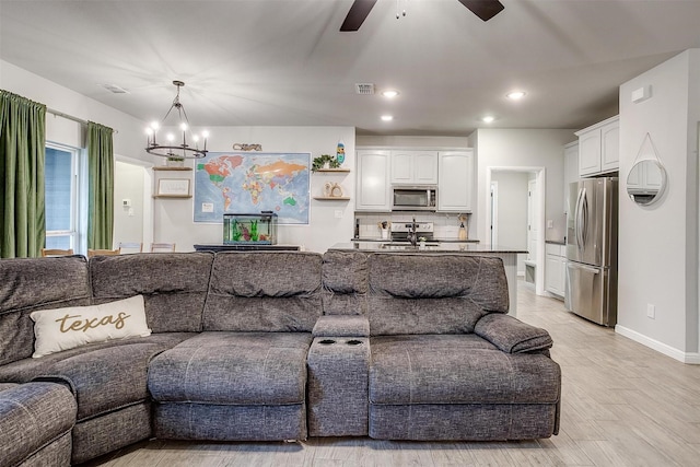 living room featuring ceiling fan with notable chandelier and light wood-type flooring