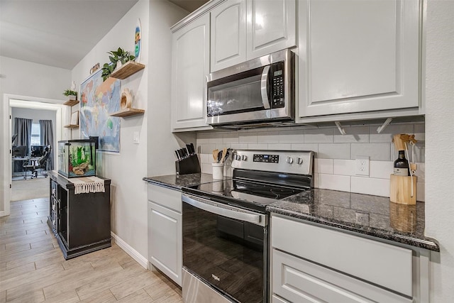 kitchen with appliances with stainless steel finishes, dark stone countertops, backsplash, white cabinets, and light wood-type flooring