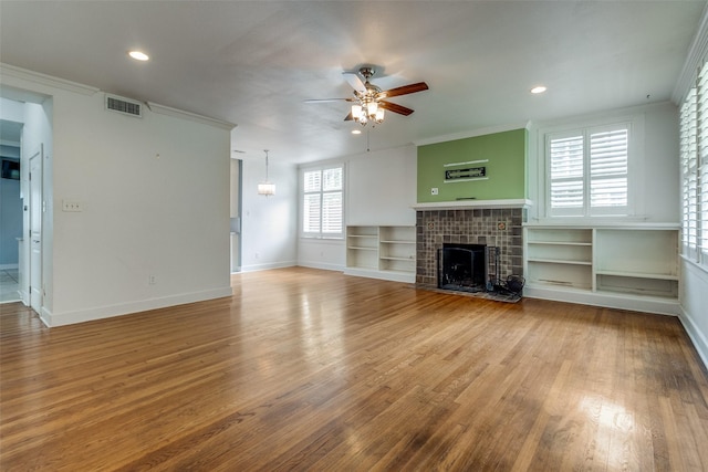 unfurnished living room featuring hardwood / wood-style floors, a fireplace, ornamental molding, ceiling fan, and built in shelves