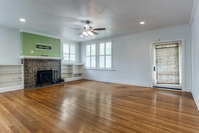 unfurnished living room with a tiled fireplace, hardwood / wood-style floors, crown molding, and ceiling fan