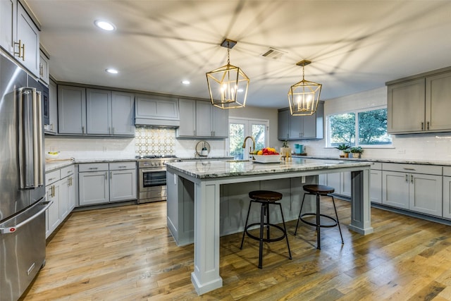 kitchen featuring light stone counters, a breakfast bar, high end appliances, light wood-style flooring, and an island with sink