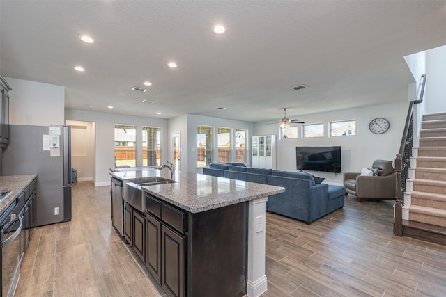 kitchen with light stone counters, sink, a center island with sink, and light wood-type flooring