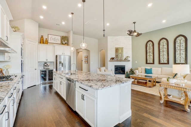 kitchen featuring decorative light fixtures, stainless steel appliances, an island with sink, and white cabinets