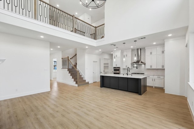 kitchen with light hardwood / wood-style flooring, hanging light fixtures, a center island with sink, wall chimney range hood, and white cabinets