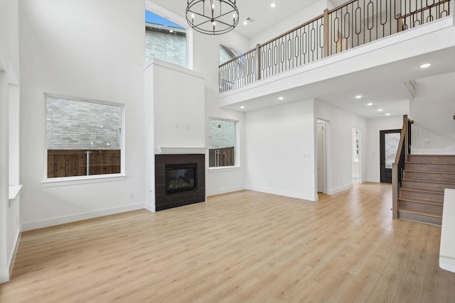 unfurnished living room featuring a tiled fireplace, a notable chandelier, a towering ceiling, and light hardwood / wood-style flooring