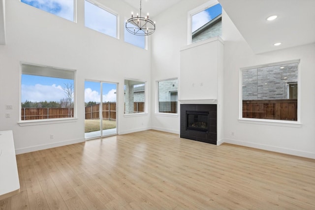 unfurnished living room featuring an inviting chandelier, a wealth of natural light, light hardwood / wood-style floors, and a high ceiling