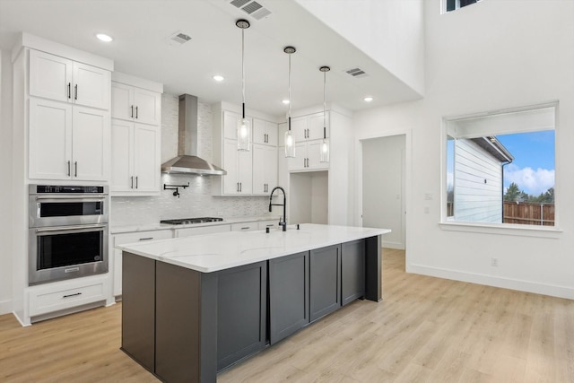 kitchen with hanging light fixtures, wall chimney exhaust hood, light stone countertops, white cabinets, and stainless steel double oven