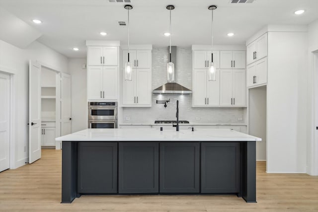 kitchen with hanging light fixtures, white cabinetry, light stone countertops, and wall chimney exhaust hood