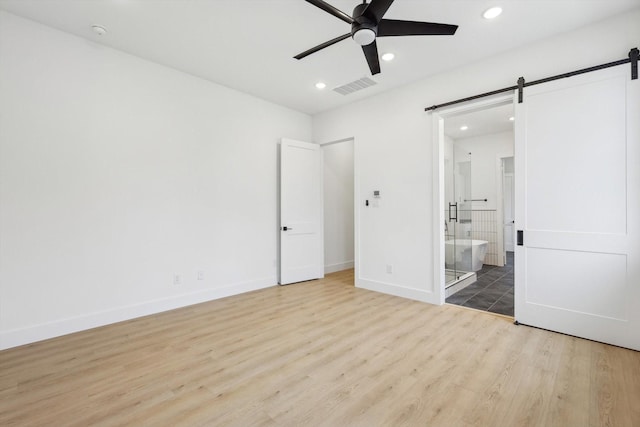 unfurnished bedroom with connected bathroom, a barn door, ceiling fan, and light wood-type flooring