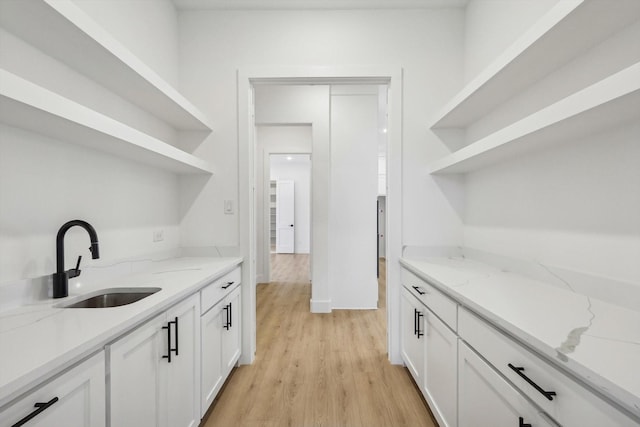 bar featuring sink, white cabinets, light stone counters, and light wood-type flooring