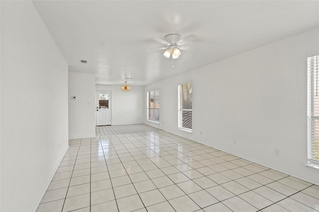 tiled spare room with ceiling fan with notable chandelier