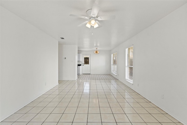 tiled spare room with ceiling fan with notable chandelier