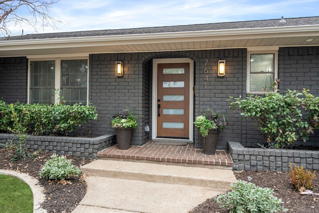 view of exterior entry with a porch and brick siding