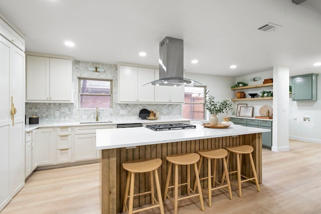 kitchen featuring island range hood, a center island, stainless steel gas stovetop, open shelves, and a sink