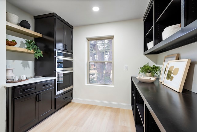 kitchen featuring light wood finished floors, open shelves, light countertops, double oven, and baseboards