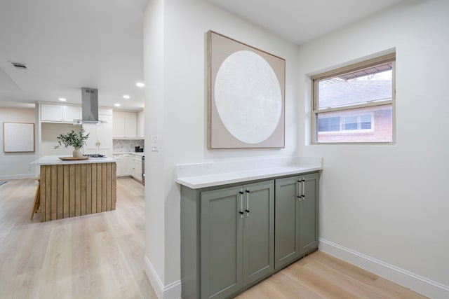 interior space featuring light wood-style flooring, visible vents, baseboards, range hood, and decorative backsplash