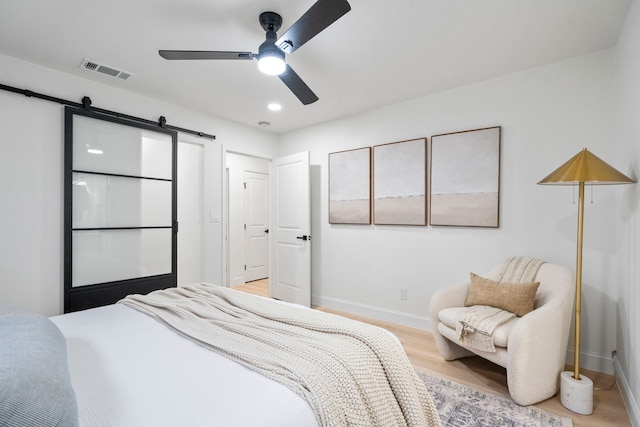 bedroom with a barn door, light wood-style flooring, visible vents, and baseboards