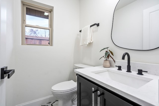 half bath featuring baseboards, vanity, and toilet