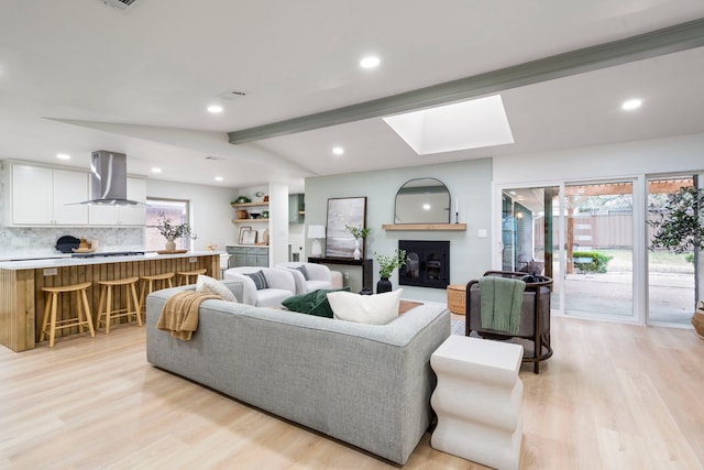 living room with light wood finished floors, lofted ceiling with skylight, a glass covered fireplace, and recessed lighting