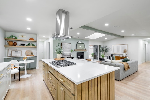 kitchen with light wood-type flooring, vaulted ceiling with skylight, island exhaust hood, and stainless steel gas stovetop