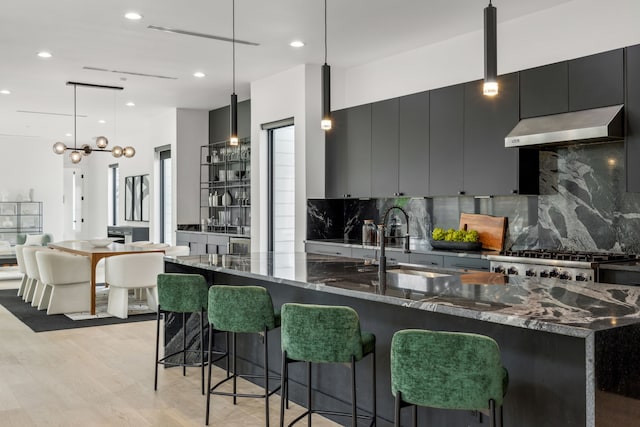 kitchen with wall chimney range hood, sink, a kitchen breakfast bar, light hardwood / wood-style floors, and decorative light fixtures