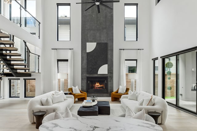 living room featuring a towering ceiling, a large fireplace, ceiling fan, and light wood-type flooring