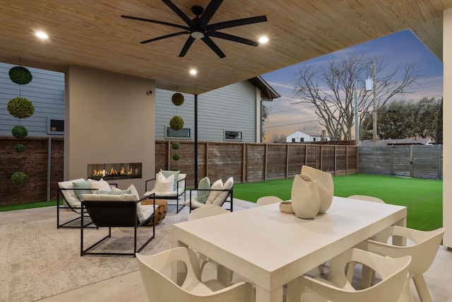 patio terrace at dusk featuring ceiling fan and an outdoor living space with a fireplace