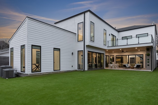 back house at dusk featuring ceiling fan, cooling unit, a yard, a patio area, and a balcony