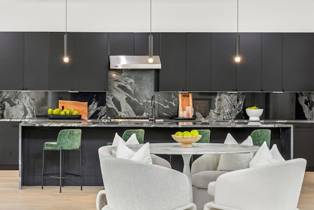 kitchen with light hardwood / wood-style flooring, a breakfast bar, hanging light fixtures, ventilation hood, and dark stone counters