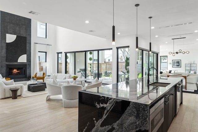 kitchen featuring sink, hanging light fixtures, a large fireplace, dark stone counters, and a kitchen island with sink