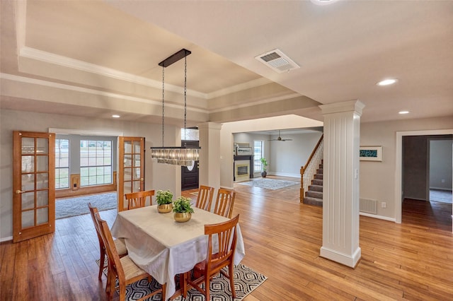 dining area with light hardwood / wood-style flooring, ornamental molding, a raised ceiling, and ornate columns