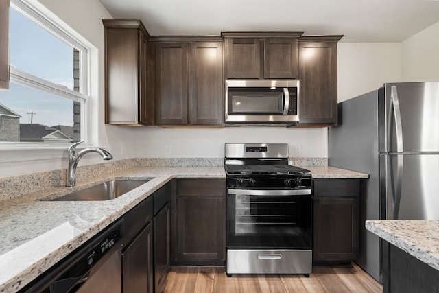 kitchen with appliances with stainless steel finishes, sink, light stone counters, and dark brown cabinets