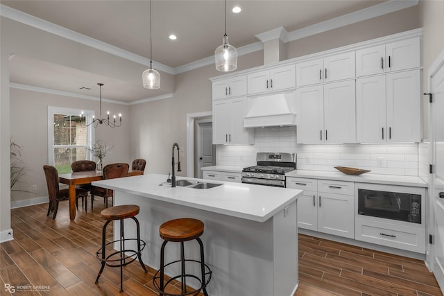 kitchen featuring black microwave, gas range, custom exhaust hood, and an island with sink